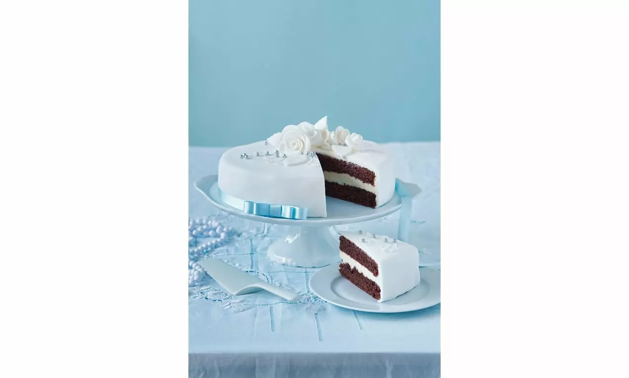 Svadobná čokoládová torta s bielym fondánom, stužkou, vrstvou krému, ozdobená marcipánovými kvetmi na podstavci a tanieri