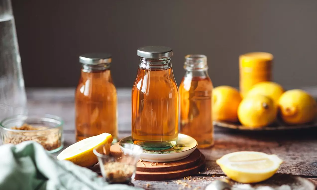 Bazový sirup v čírych sklenených fľašiach s kovovými uzávermi, zlatistý odtieň, na drevenom stole obklopený citrónmi a cukrom