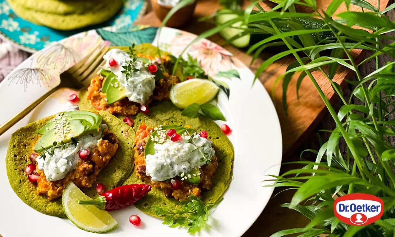 Na bielom tanieri zelené taco placky s tofu praženicou, kopčekom jemného bieleho krému, avokádom, granátovým jablkom a limetkou