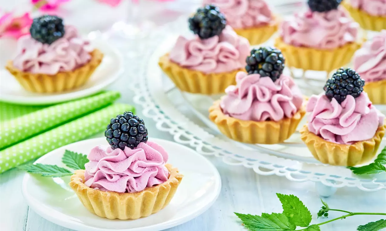 Mini tartaletky s čučoriedkovým krémom zdobené čerstvou černicou na bielom servírovacom a dezertnom tanieriku