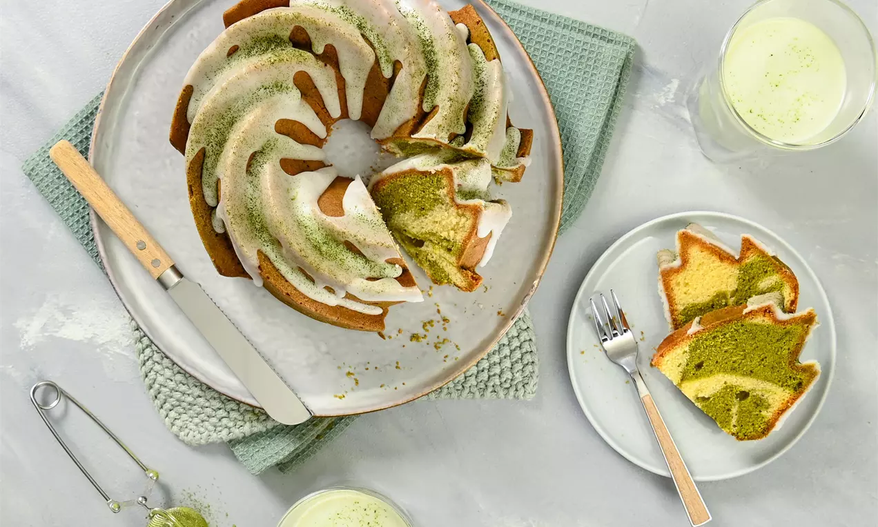 Matcha bábovka jemne zelenkavá s mramorovaným vzorom, zdobená bielou polevou na keramickom tanieri vedľa mäkkej ozdobnej utierky