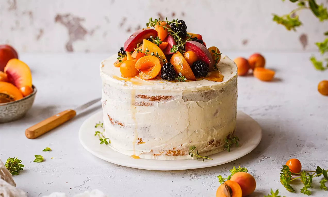 biela vanilková torta na bielom stole a bielom tanieriku, ozdobená ovocím a poliatá sirupom