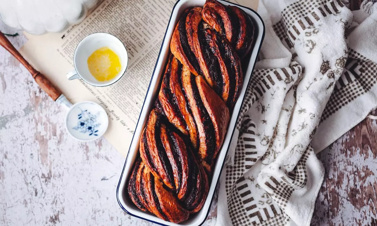 Zamotaný dvojfarebný múčnik vo forme na biskupský chlebíček na drevenej bielej doske s ľanovou utierkou po pravej strane