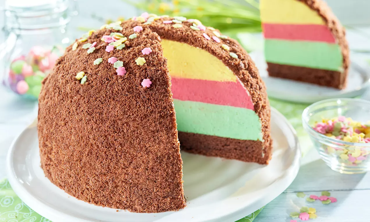 Guľovitá torta s čokoládovými strúhankovými drobkami, vrstvami žltej, ružovej a zelenej krémovej náplne, ozdobená farebnými kvietkami