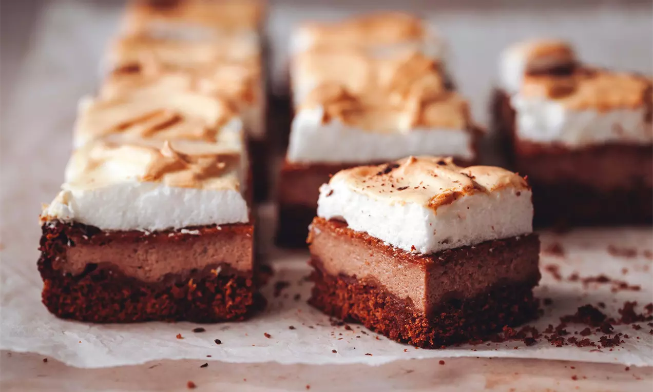 Čokoládový zákusok s tmavohnedým korpusom, krémovou čokoládovou vrstvou a nadýchanou zlatistou meringue polevou na papieri na pečenie