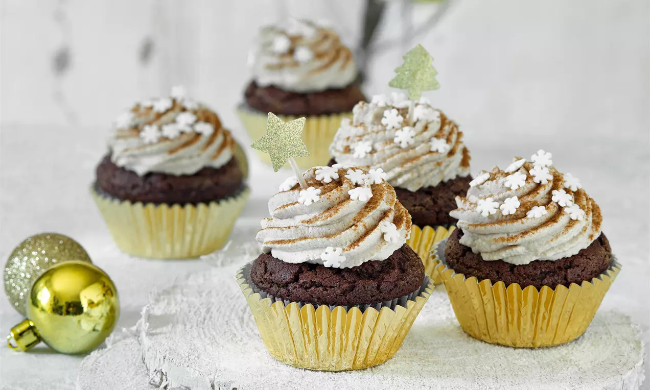 Vianočné perníkové cupcakes v zlatých košíčkoch s nadýchaným svetlohnedým škoricovým krémom, ozdobené cukrovými vločkami a hviezdičkami