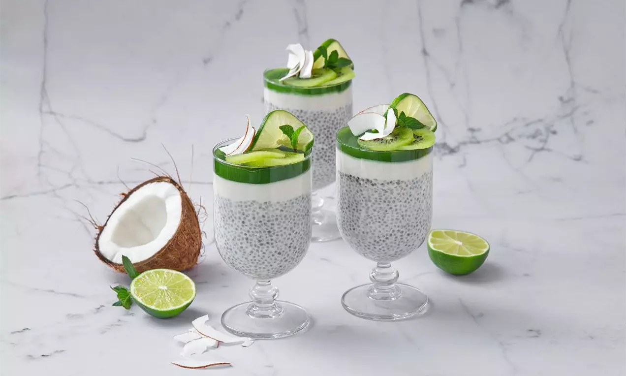 Poháre s chia pudingom šedej farby, bielou kokosovou vrstvou a zeleným matcha želé zdobené limetkovým plátkom a lístky mäty na mramore