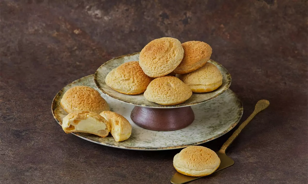 Odpaľované guličky so zlatistou chrumkavou krustou na rustikálnom keramickom tanieri, jedna rozkrojená s jemným vanilkovým krémom vo vnútri