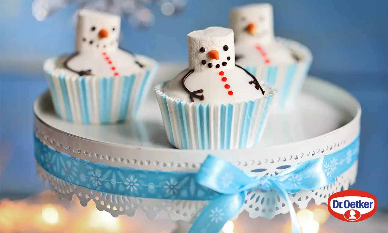 Marshmallow snehuliaci s čokoládovými rukami, očami a úsmevom, na modro-bielych papierových košíčkoch, zdobené červenými bodkami tlačidiel