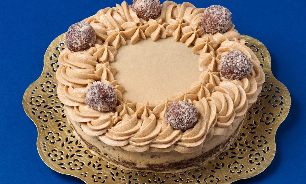 Kapucínska torta s hladkým karamelovým vrchom, obklopeným krémovými vírmi a zdobená guľôčkami so škoricovou posýpkou na zlatom podnose