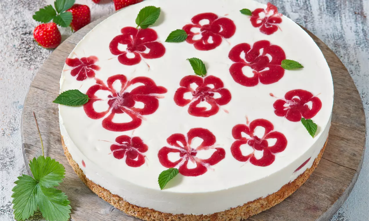 Orechová torta s jahodami na drevenom podnose, bielej krémovej textúre s červenými jahodovými vzormi kvetov, obklopená lístkami mäty