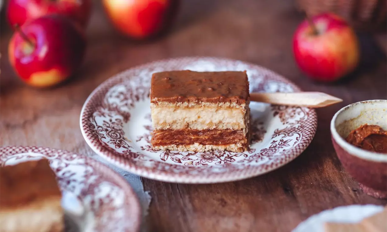 vrstvený dezert so svetlým korpusom svetlou a hnedou karamelovou vrstvou a karamelovou polevou servírovaný na zdobenom dezertnom tanieriku na drevenej doske