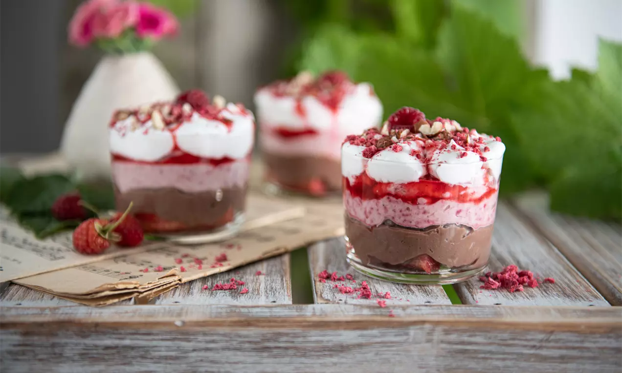 BB pohár s mascarpone v priehľadnom skle, navrstvený kakaovým krémom, ružovým malinovým pyré, šľahačkou, malinami a drvenými orechmi
