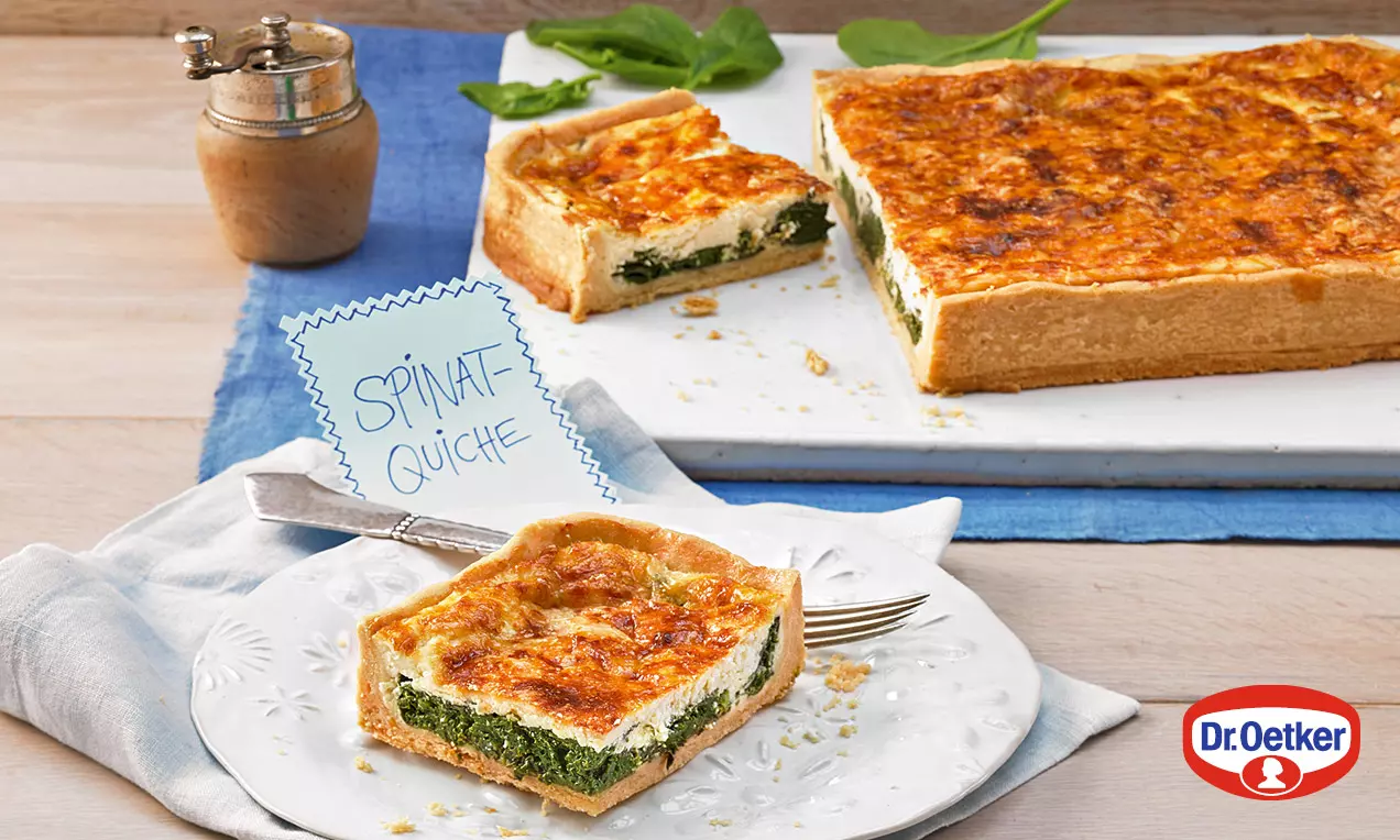Špenátový quiche s krehkým svetlohnedým cestom, zelenou špenátovou vrstvou a zlatistou syrovo-smotanovou náplňou na bielom tanieri