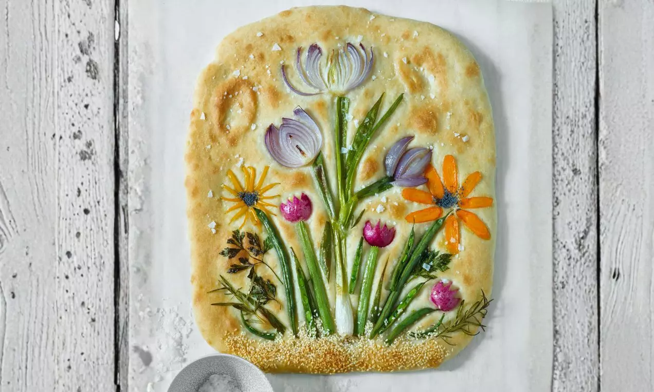 Zlatistá focaccia s textúrou jemne chrumkavého cesta, ozdobená farebnými zeleninovými kvetmi z cibule, papriky, reďkovky a byliniek