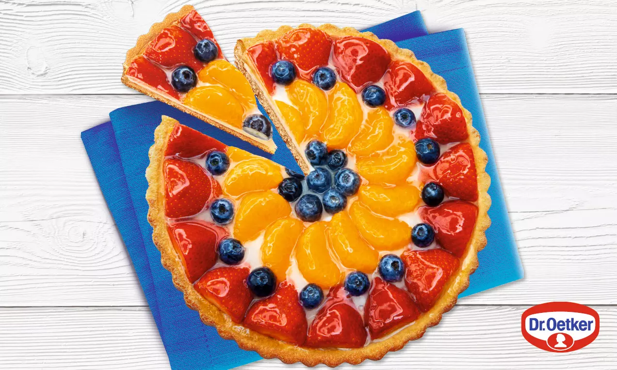 Farebná okrúhla torta s lesklým ovocím v želé, usporiadaným do kruhov červenej, oranžovej a modrej na chrumkavom zlatistom korpuse