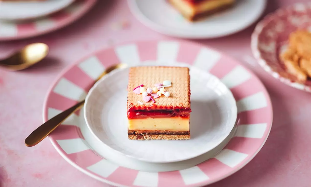 obdĺžnikový dezert s vrstvou sušienok, vanilkovým pudingom a ovocným rozvarom na ozdobnom bielo-ružovom dezertnom tanieriku