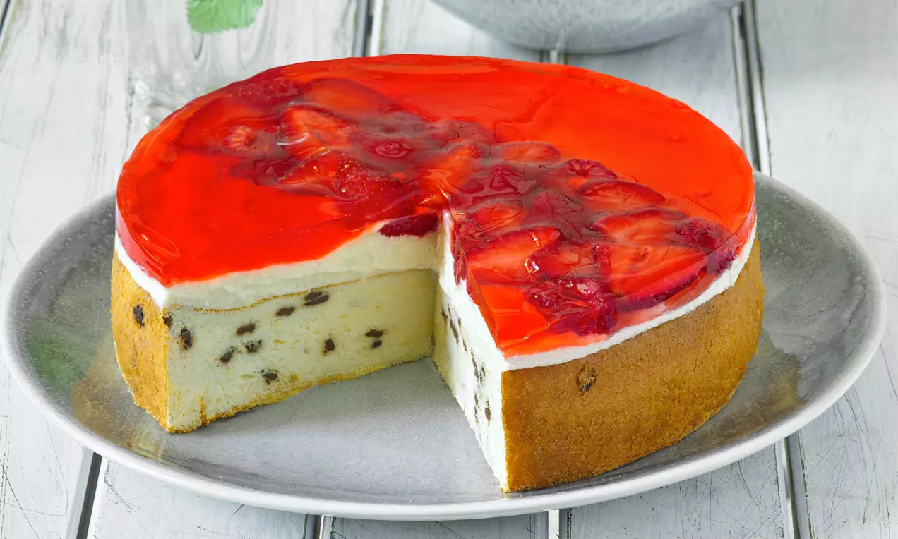 Jogurtová jahodová torta s červenou želatínou a plátkami jahôd na vrchu, krémovou bielou plnkou s hrozienkami na svetlosivom tanieri