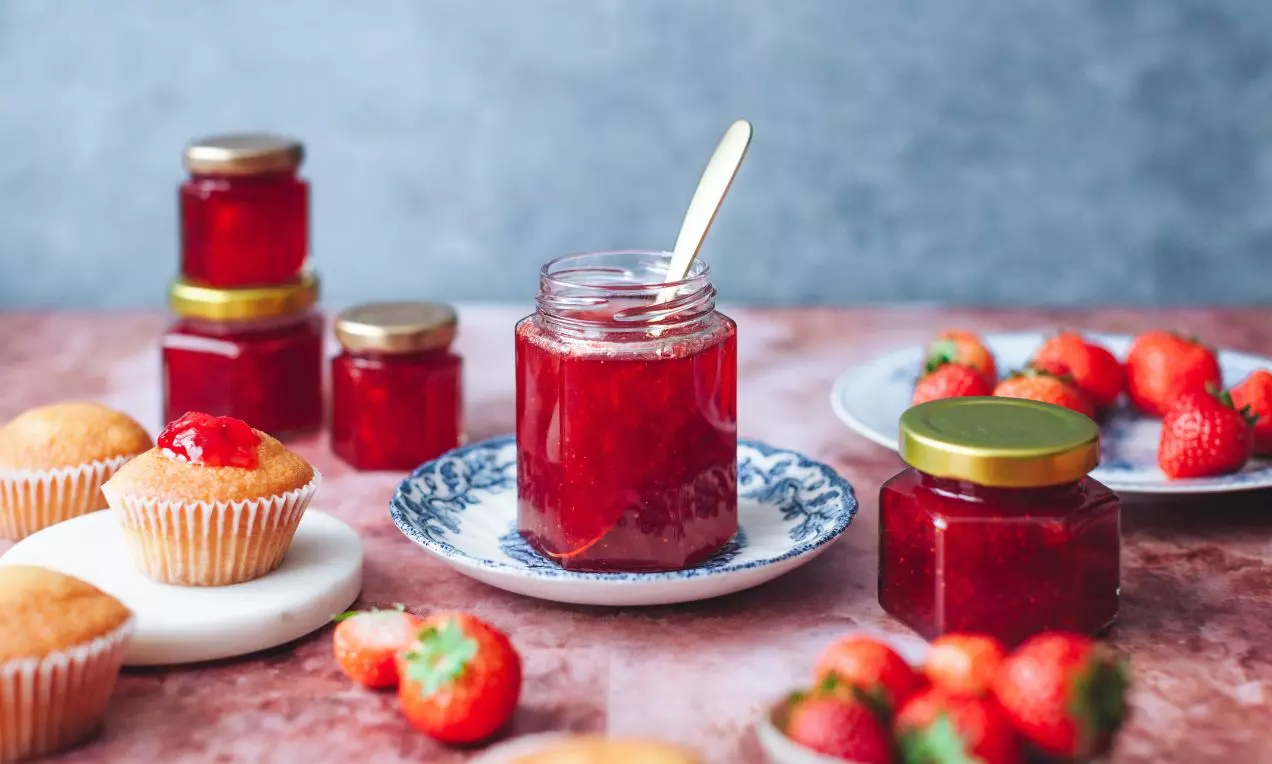Extra ovocný jahodový džem sýtočervenej farby s hladkou lesklou textúrou v sklenenom pohári so zlatou lyžičkou na keramickej tácke