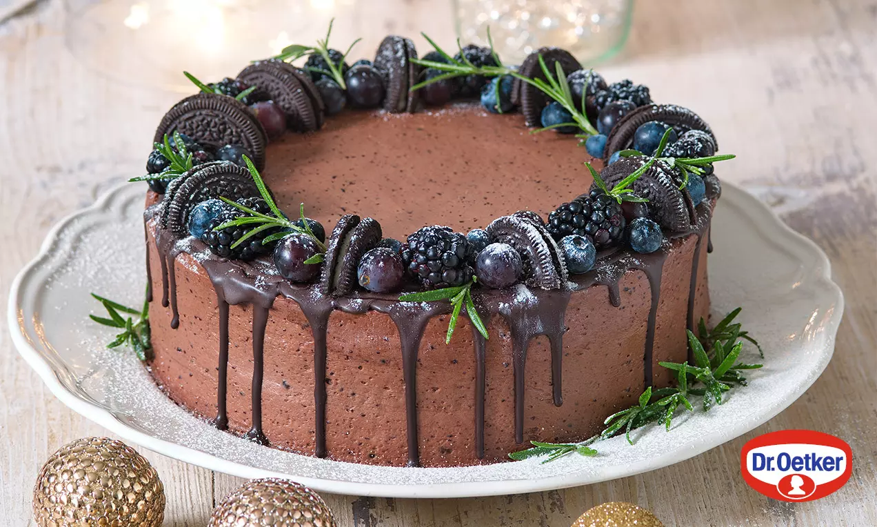 Dvojfarebná BB torta s čokoládovou polevou stekajúcou po bokoch, zdobená černicami, čučoriedkami, Oreo kúskami a zelenými lístkami na bielom tanieri