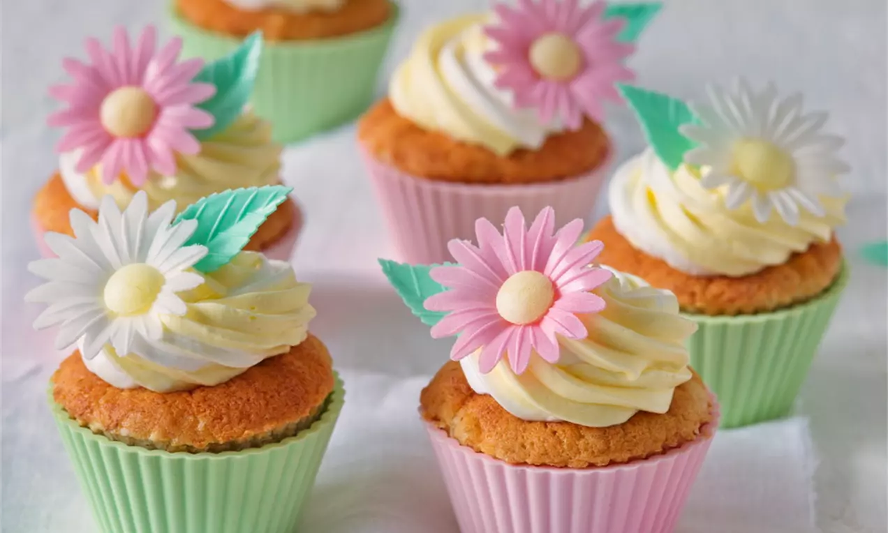 Banánové cupcakes v pastelových papierových košíčkoch, s nadýchaným krémom a ozdobou z farebných jedlých sedmokrások a lístkov