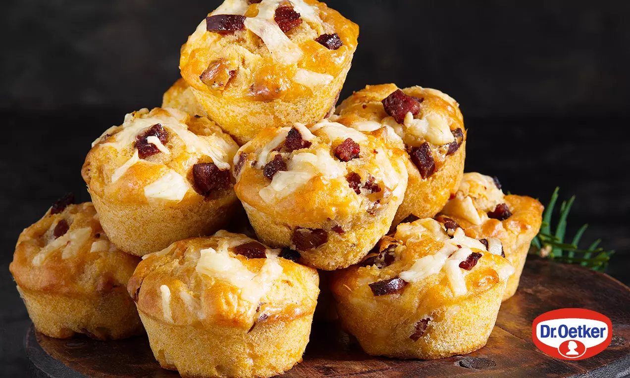 Zlatohnedé muffiny s chrumkavými kúskami slaniny a syrovou posýpkou, naukladané na drevenom podnose s tmavým pozadím